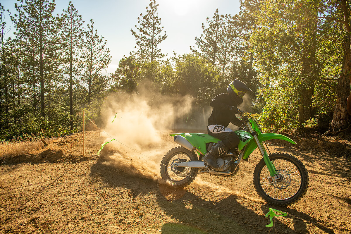 Three-quarter front angle of a person riding a motorcycle past some trees off-road.