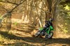 Three-quarter front angle of a person riding a motorcycle around a tree off-road.