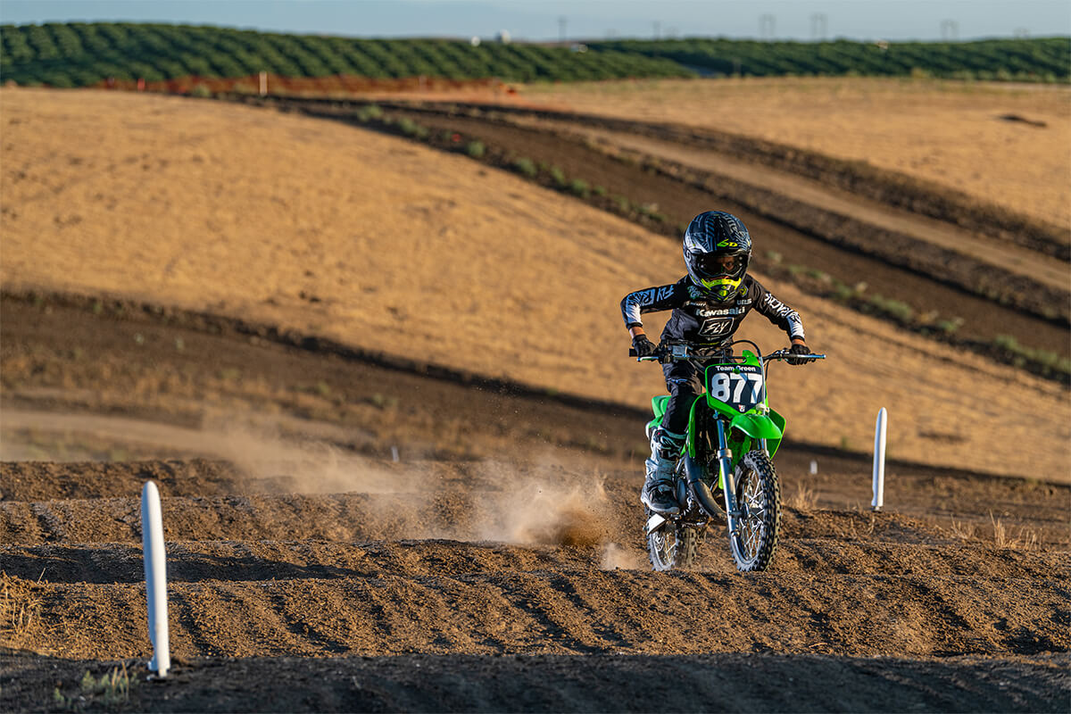 Three-quarter front angle of a child riding a motorcycle through the whoops on a track.
