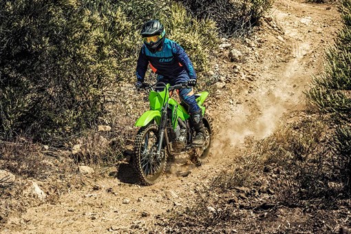 Three-quarter front angle of a person riding a green motorcycle off-road. opens in a new window