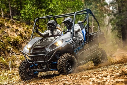 Three-quarter front angle of a person and passenger driving a side x side off-road down hill. opens in a new window