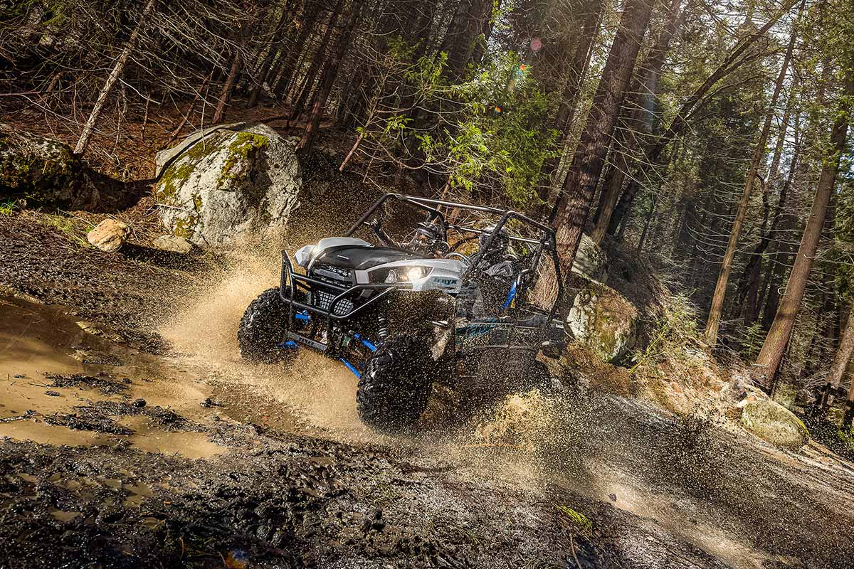 Three-quarter front angle of a person and passenger driving a side x side off-road through a puddle.