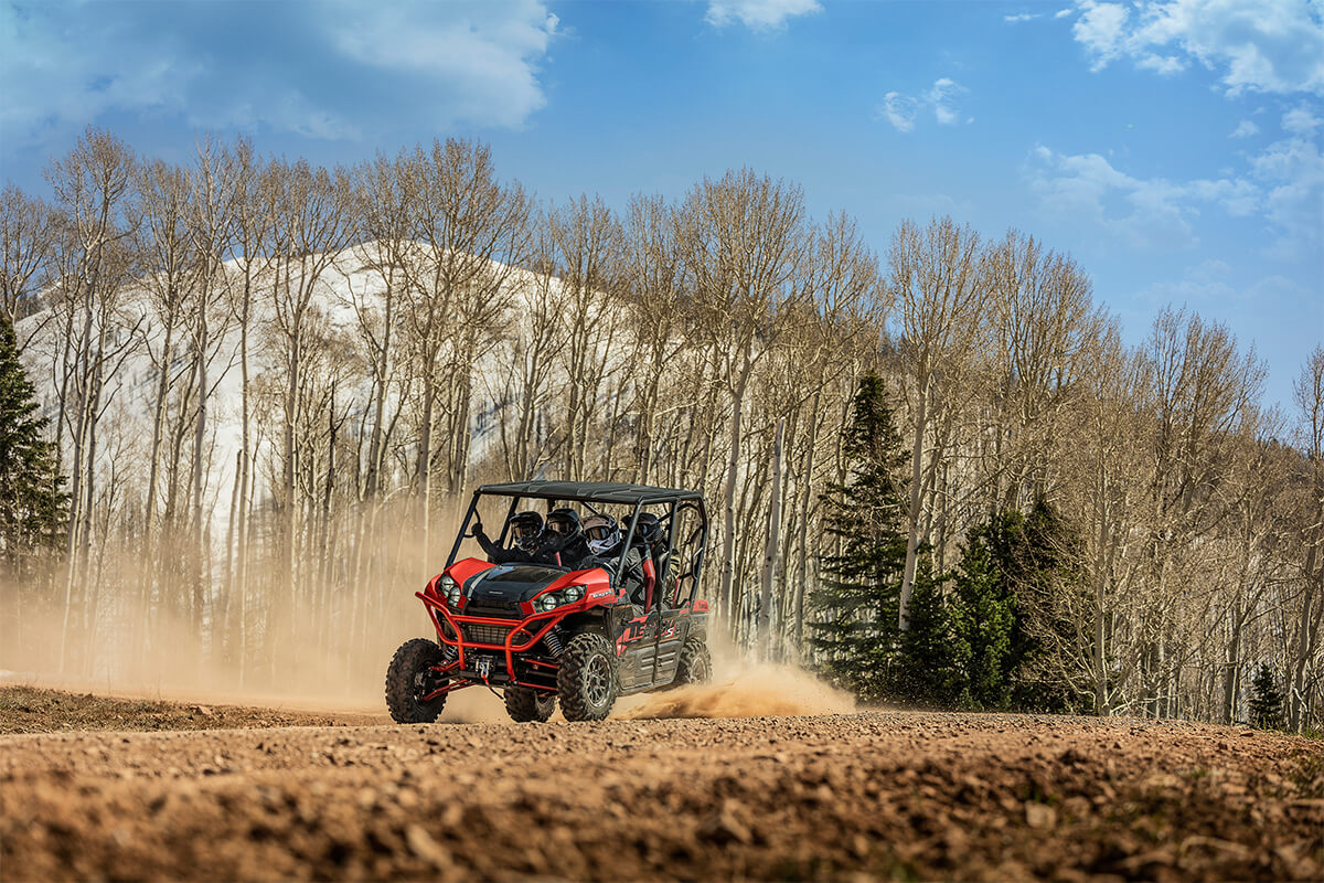 Three-quarter front angle of a person and passengers driving a side x side off-road.