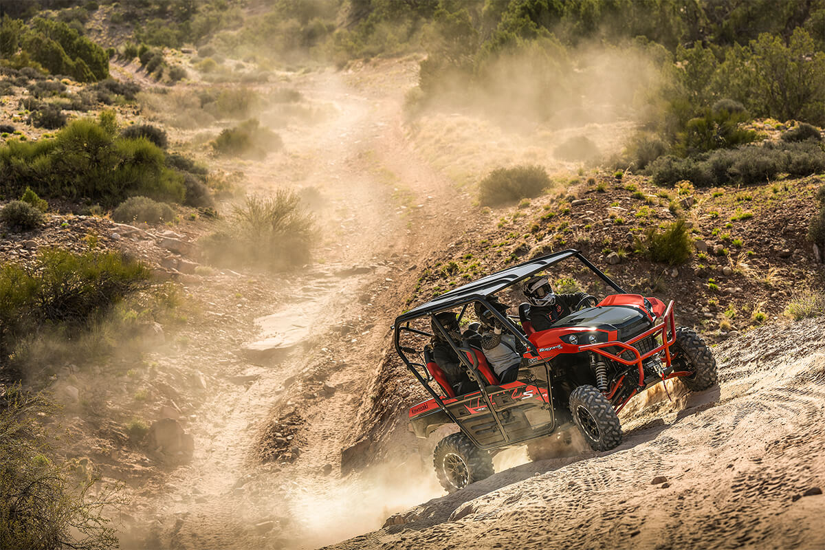 Side angle of a person and passengers driving a side x side off-road up hill.