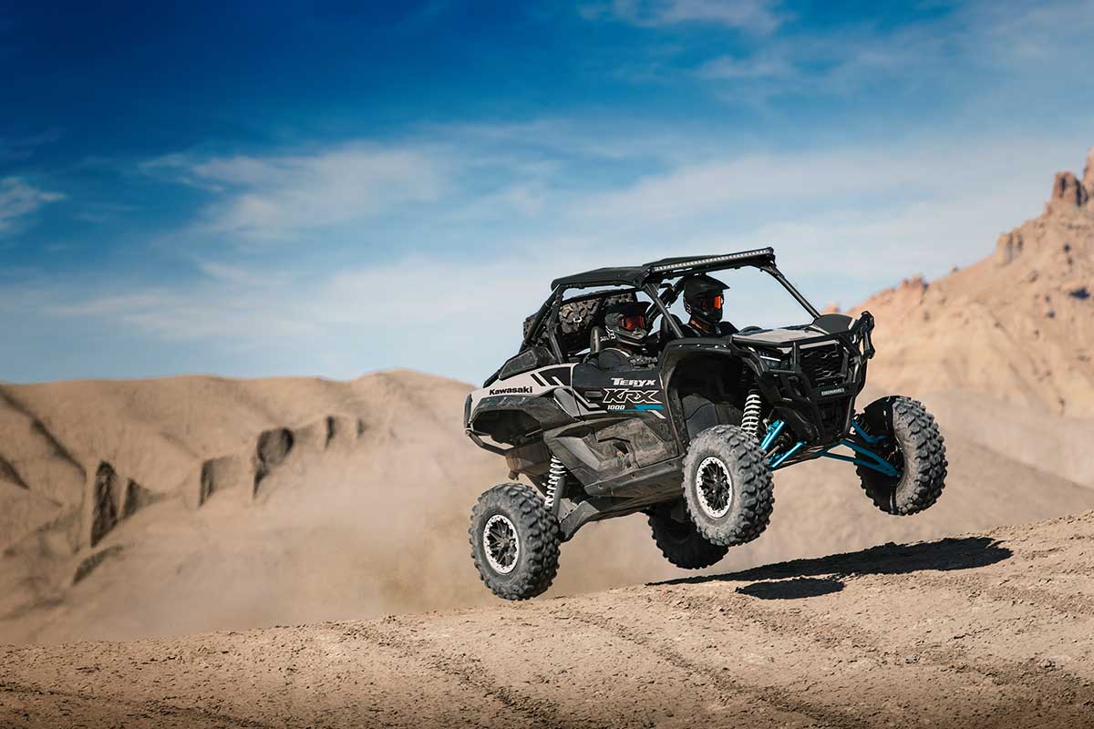 Three-quarter front angle of a person and passenger driving a side x side off-road.