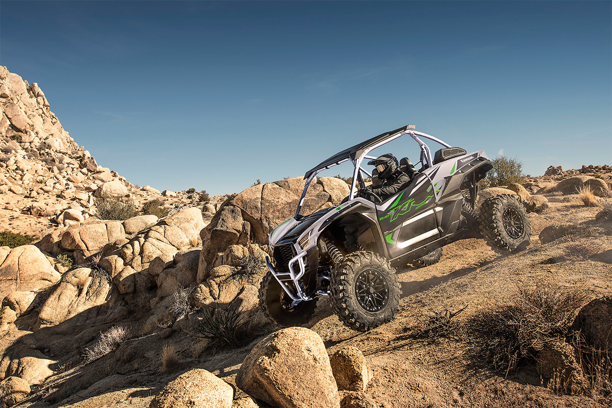 Three-quarter front angle of a person driving a side x side off-road down hill.