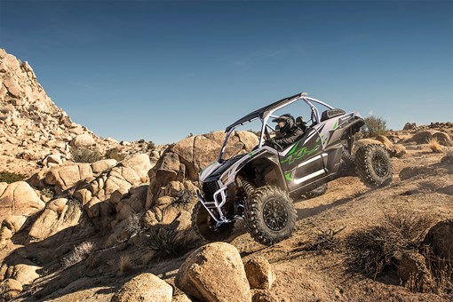 Three-quarter front angle of a person driving a side x side off-road down hill. opens in a new window