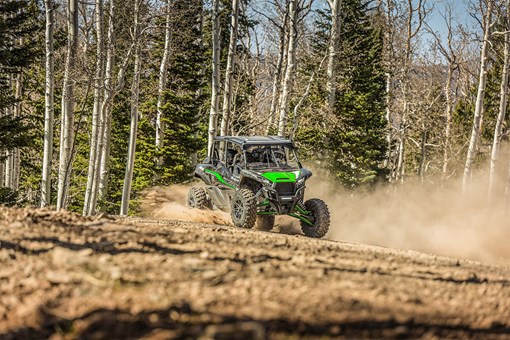 Front angle of a person and passengers driving a side x side off-road through trees. opens in a new window