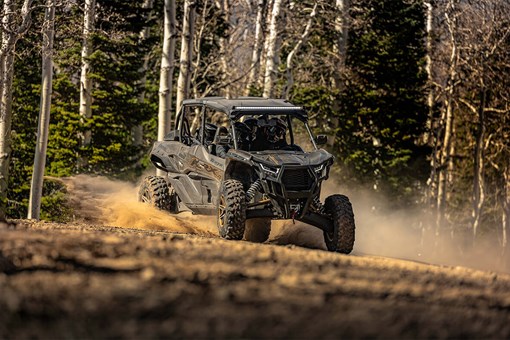 Three-quarter front angle of a person and passengers driving a side x side off-road through trees. opens in a new window