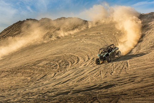 Three-quarter front angle of a person driving a side x side off-road down hill. opens in a new window