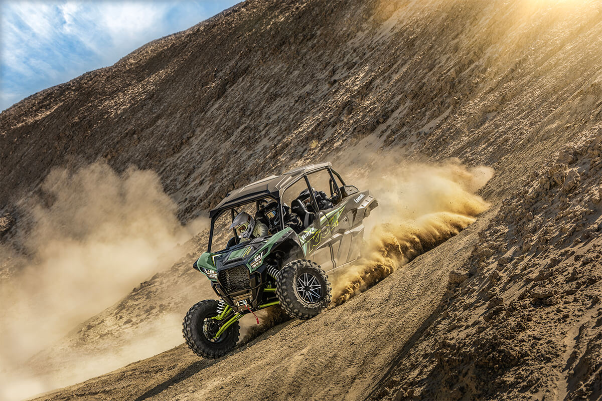 Three-quarter front angle of a person and passengers driving a side x side off-road down hill.