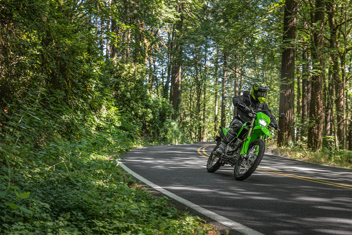 Three-quarter front angle of a person riding a motorcycle while surrounded by trees.