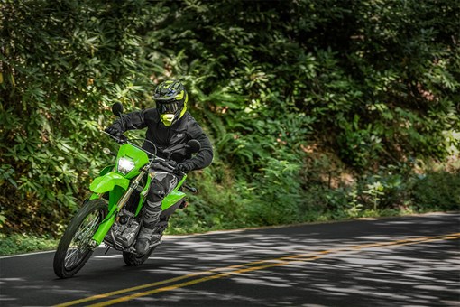 Three-quarter front angle of a person riding a green motorcycle on a highway. opens in a new window