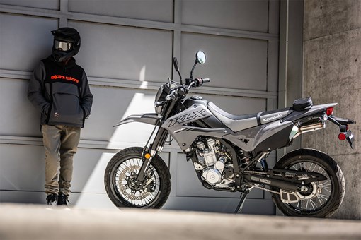 Side angle of a person standing next to a motorcycle in front of a garage. opens in a new window