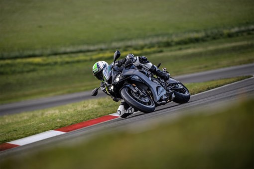 Three-quarter front angle of a person riding a motorcycle through a corner on a track with their leg out. opens in a new window