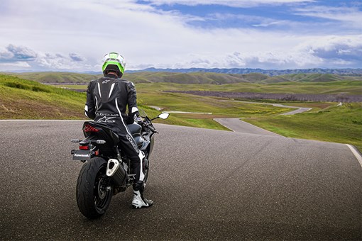 Rear angle of a person sitting on a motorcycle on a track. opens in a new window
