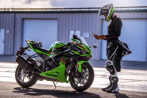 Side angle of a person standing in front of a motorcycle. opens in a new window