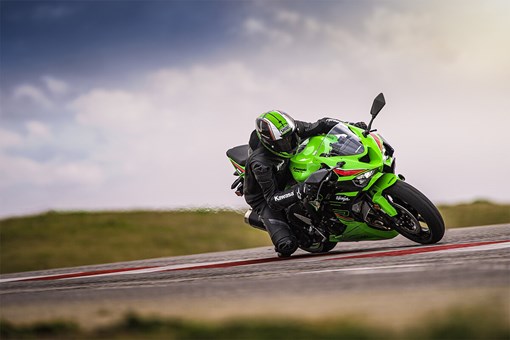 Three-quarter front angle of a person on a green motorcycle leaning into a corner on a track. opens in a new window