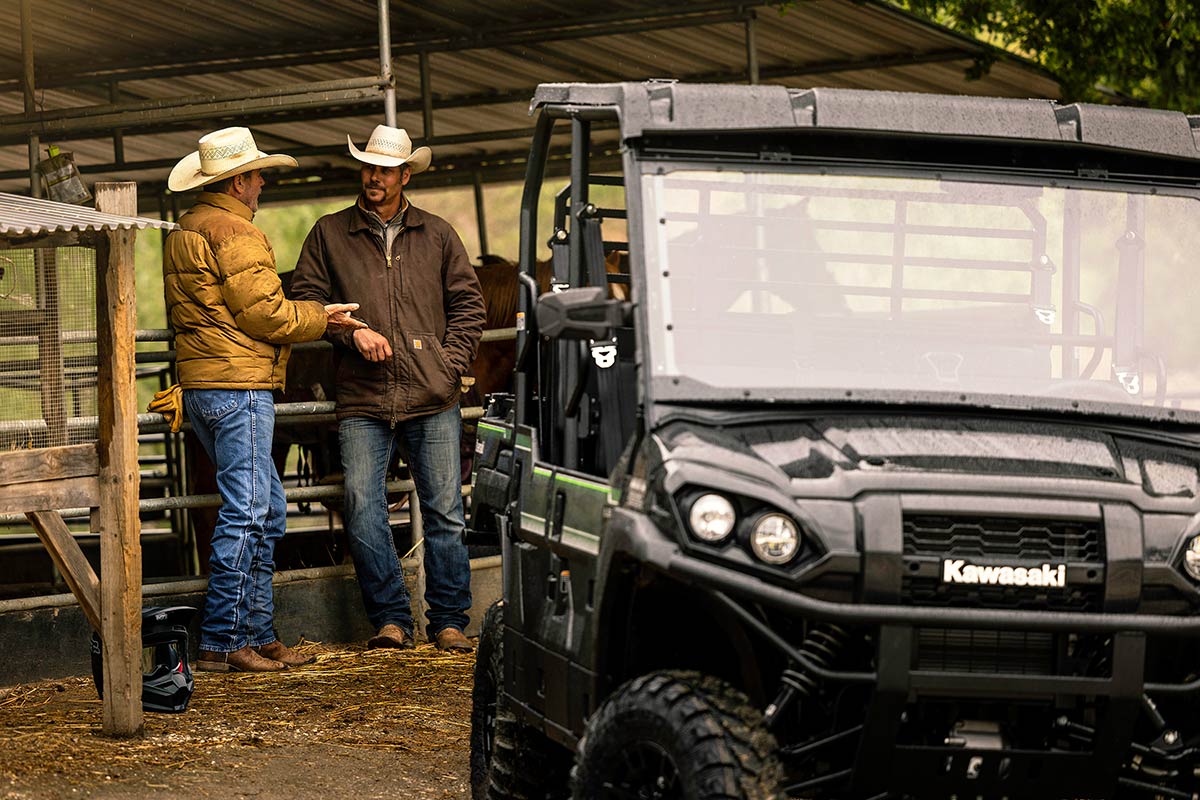Three-quarter front angle of two people talking behind a parked side x side.