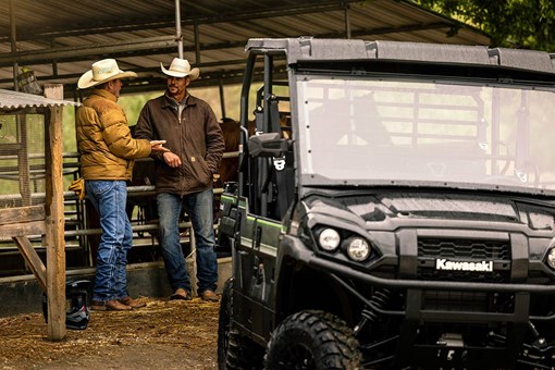 Three-quarter front angle of two people talking behind a parked side x side. opens in a new window