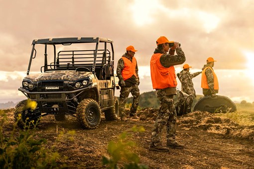 Three-quarter front angle of four people standing next to a parked side x side off-road. opens in a new window