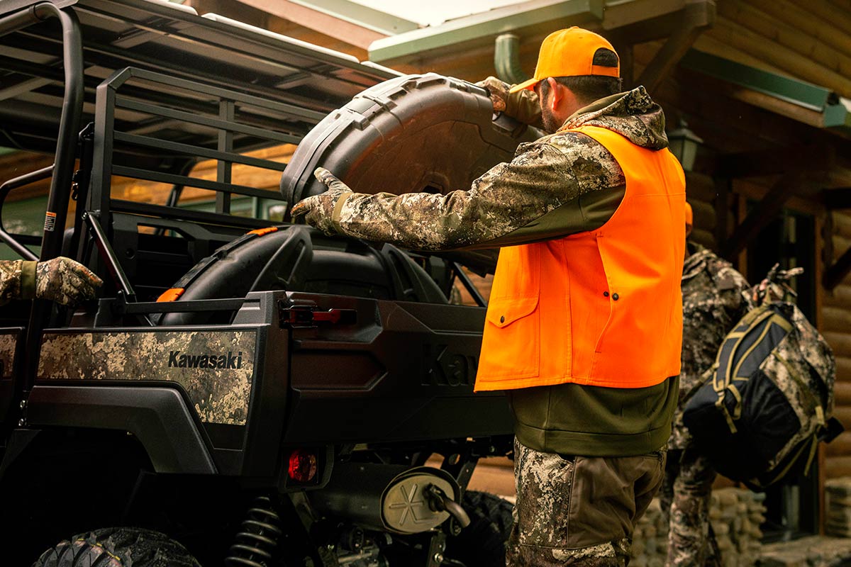 Three-quarter rear angle of a person loading a side x side near a cabin.