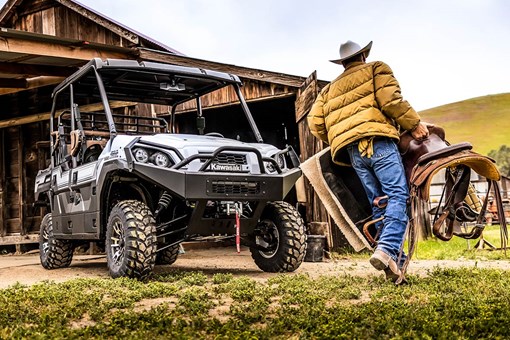 Three-quarter front angle of a person loading a side x side in front of a barn. opens in a new window