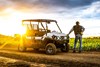 Three-quarter front angle of a person standing next to a side x side off-road with a sunset behind it.