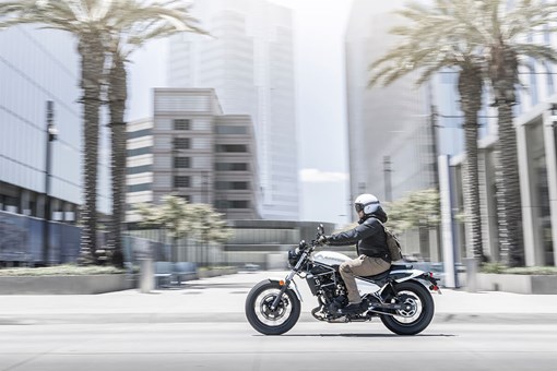 Profile angle of a person riding a motorcycle through a city. opens in a new window