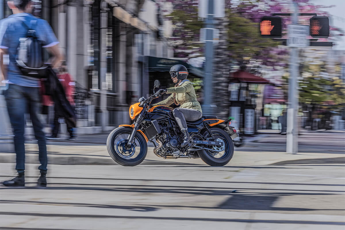 Profile angle of a person riding an orange motorcycle through the city.
