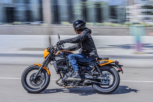 Profile angle of a person riding an orange motorcycle in the city. opens in a new window