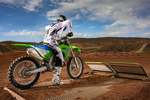 Three-quarter rear angle of a person sitting on a motorcycle at the starting gate of a dirt track. opens in a new window