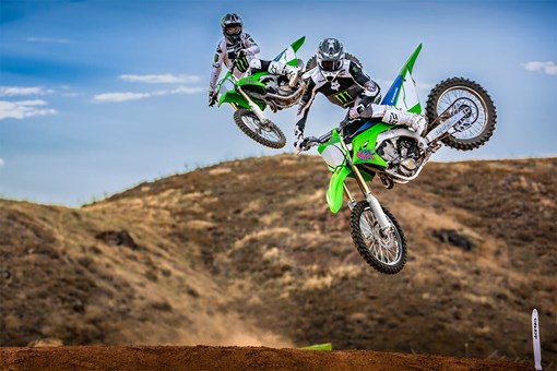Three-quarter front angle of two riders making a jump on their motorcycles off-road. opens in a new window