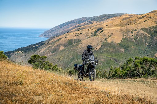 Three-quarter front angle of a person riding a motorcycle on a dirt trail. opens in a new window