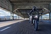 Front angle of a person riding a motorcycle over a bridge.