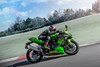 Side angle of a person riding a green motorcycle on a racetrack.