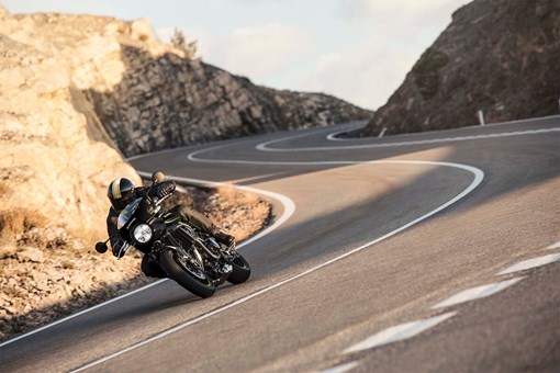 Front angle of a person riding a motorcycle around a bend in a road. opens in a new window