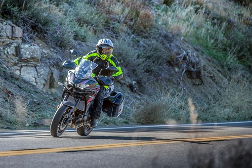 Three-quarter front angle of a person riding a black motorcycle on a road. opens in a new window