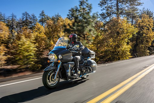 Three-quarter front angle of a person riding a black motorcycle on a road. opens in a new window
