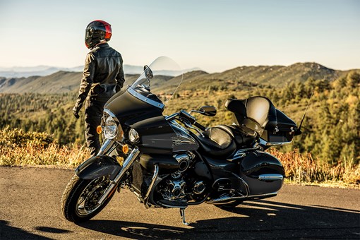 Side angle of a person standing next to a parked motorcycle. opens in a new window