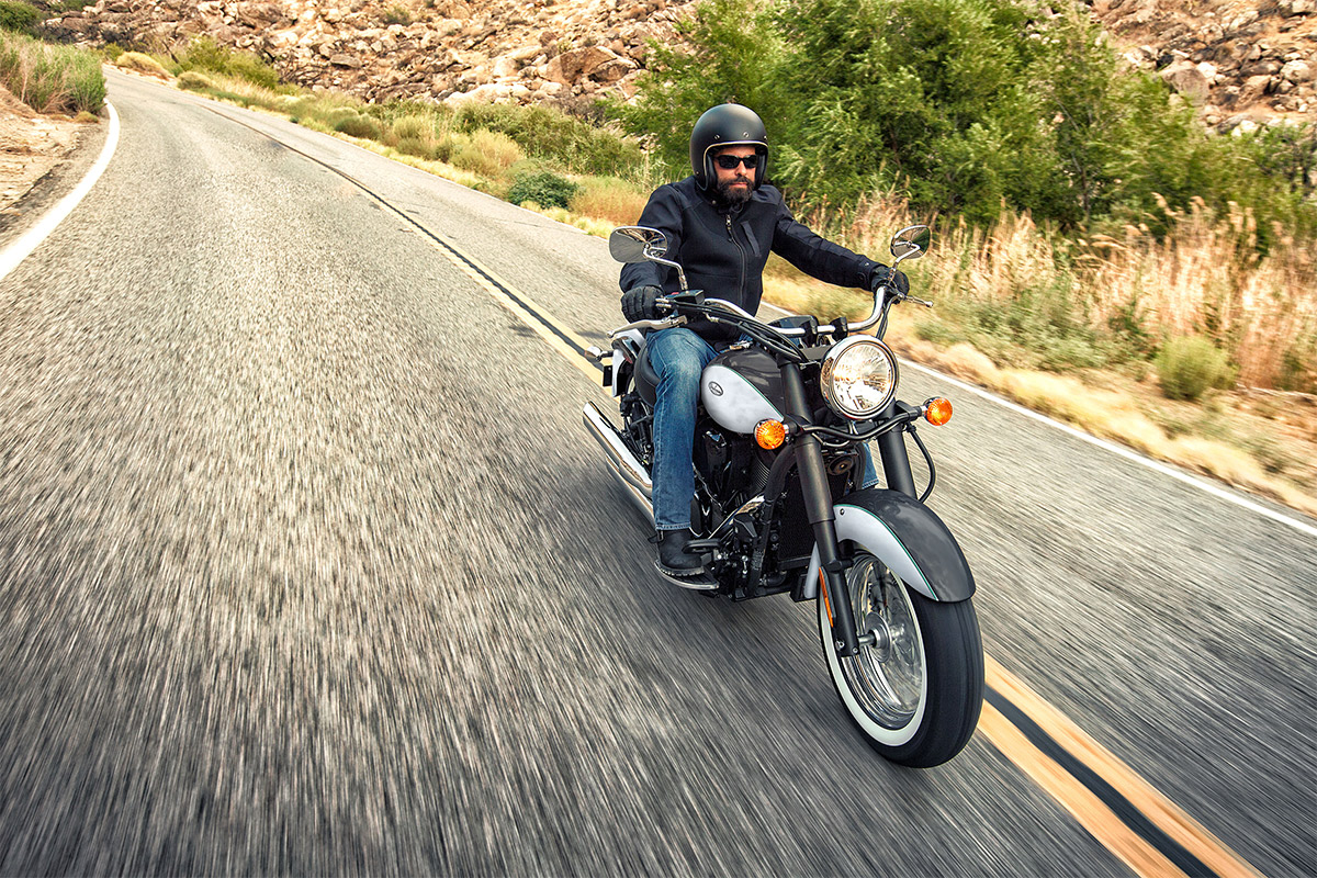Front angle of a person riding a silver motorcycle on a road.