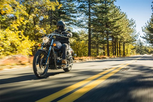 Three-quarter front angle of a person riding a gray motorcycle on a road. opens in a new window