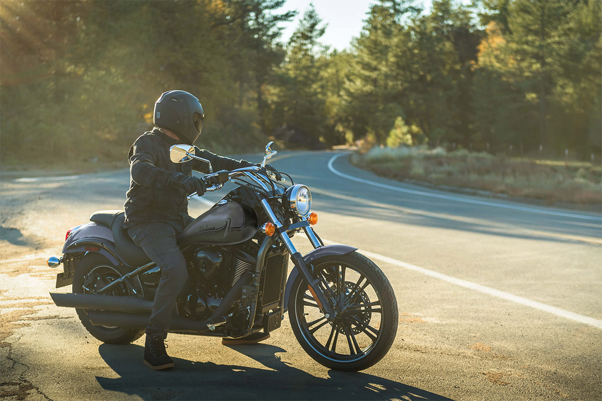 Side angle of a person on a parked motorcycle near a road.