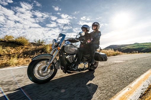 Side angle of a person and passenger riding a motorcycle on a road. opens in a new window