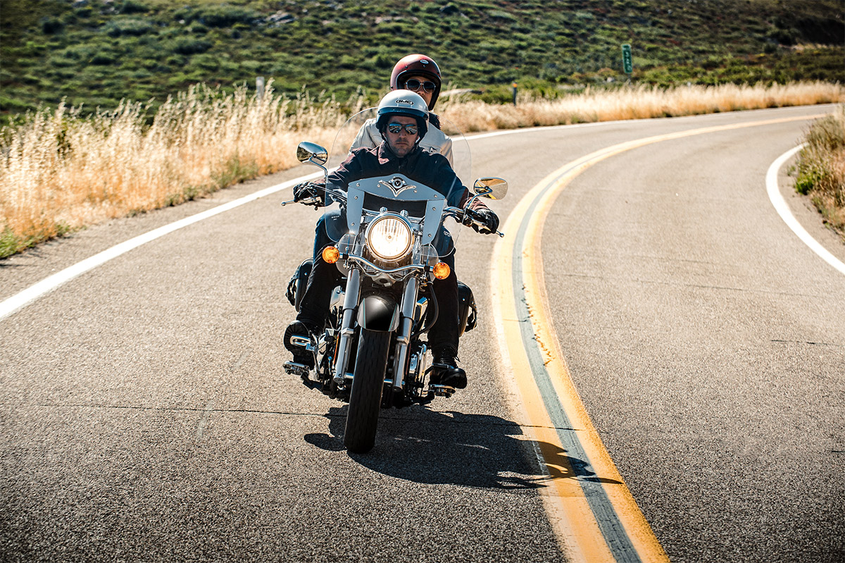 Front angle of a person and passenger riding a motorcycle on a road.
