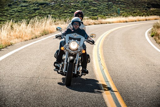 Front angle of a person and passenger riding a motorcycle on a road. opens in a new window