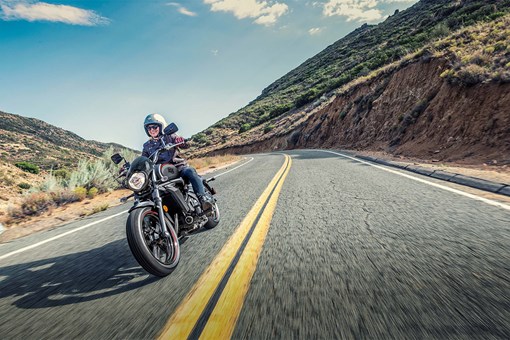 Three-quarter front angle of a person riding a motorcycle on a road. opens in a new window