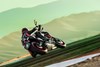 Three-quarter rear angle of a person riding a motorcycle on a racetrack.