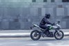 Side angle of a person riding a green motorcycle on a street.