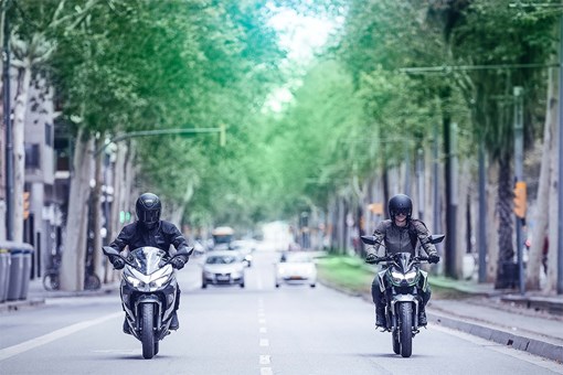 Front angle of two people riding motorcycles on a street. opens in a new window